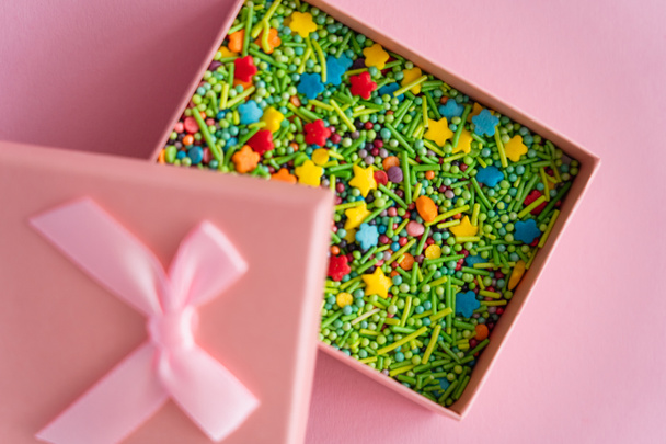 Top view of colorful sprinkles in gift box on pink background  - Photo, Image