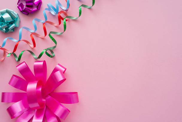 Top view of gift bows and serpentine on pink background with copy space  - 写真・画像