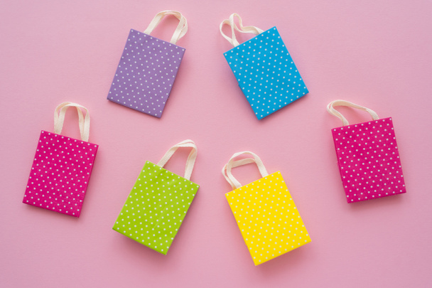 Vista superior de pequeñas bolsas de compras de colores sobre fondo rosa  - Foto, imagen