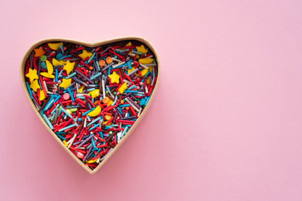 Top view of sweet sprinkles in heart shaped gift box on pink background  - Fotó, kép