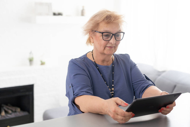 Χαρούμενη χαμογελαστή ηλικιωμένη γυναίκα με ψηφιακό tablet υπολογιστή που έχει βιντεοκλήση στο σπίτι. Γιαγιά χαμογελώντας απολαμβάνοντας κοινωνική απόσταση εικονική οικογενειακή σε απευθείας σύνδεση συνομιλία συνάντηση - Φωτογραφία, εικόνα