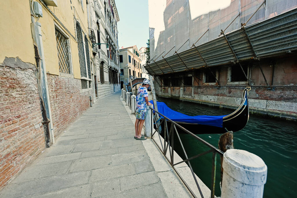 Boy stand near canal with covered gondola in Venice, Italy.  - Foto, Imagem