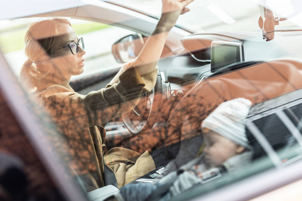 Mère se concentre sur la conduite d'une voiture familiale faisant des courses pendant que son bébé dort dans un siège auto près de son site - Photo, image