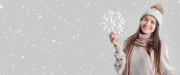 Jeune femme souriante en vêtements d'hiver tenant grand flocon de neige sur fond gris avec espace pour le texte - Photo, image