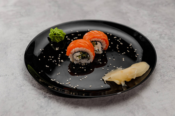 Két adag sushi lazaccal és uborkával, vossabi szósszal és gyömbérrel, fekete tálcán. Oldalnézet - Fotó, kép