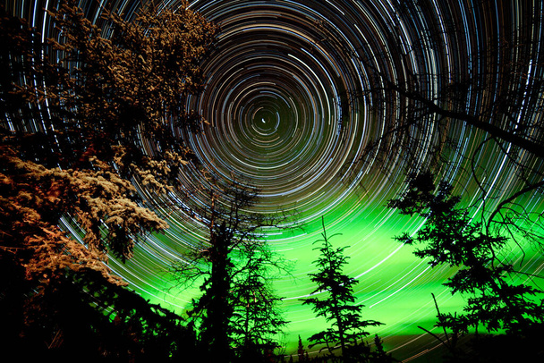 Astrophotography star trails with green glowing display of Northern Lights or Aurora borealis over boreal forest or taiga of Yukon Territory, Canada - Photo, Image