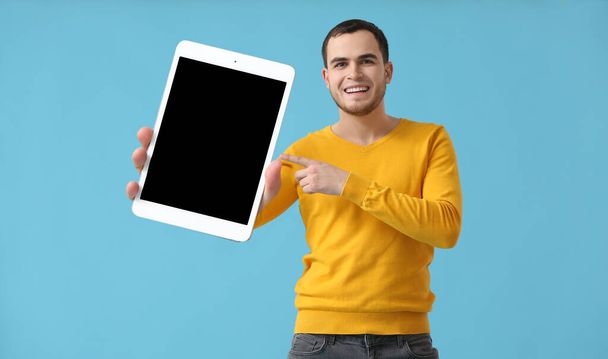 Handsome young with big tablet computer on light blue background - Fotó, kép