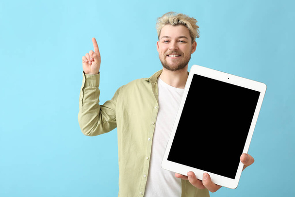 Handsome young with big tablet computer pointing at something on light blue background - Photo, Image