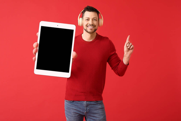 Человек с большим планшетным компьютером и наушниками, указывающим на что-то на красном фоне - Фото, изображение