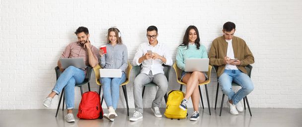 Estudiantes con dispositivos modernos sentados cerca de la pared de luz - Foto, imagen