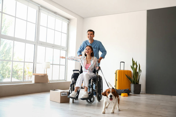 Szczęśliwy młody człowiek z żoną i psem na wózku inwalidzkim w nowym mieszkaniu w dniu przeprowadzki - Zdjęcie, obraz