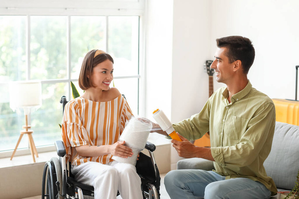 Mladý muž se svou ženou na invalidním vozíku balení věci v místnosti v den stěhování - Fotografie, Obrázek