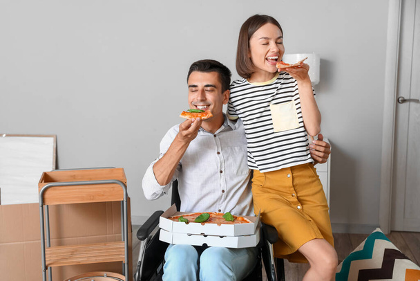 Genç bir kadın ve kocası taşındıkları gün tekerlekli sandalyede pizza yiyorlar. - Fotoğraf, Görsel