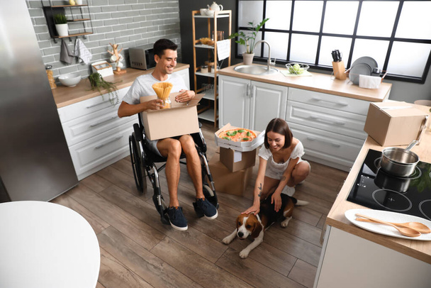 Młoda kobieta z mężem na wózku inwalidzkim i psem w kuchni w dniu przeprowadzki - Zdjęcie, obraz