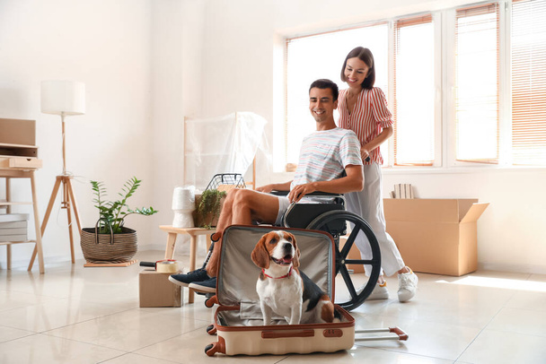Young woman with her husband in wheelchair and dog in suitcase on moving day - Photo, Image