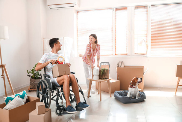 Молодая женщина с мужем в инвалидном кресле и собакой упаковывает вещи в комнате в день переезда - Фото, изображение