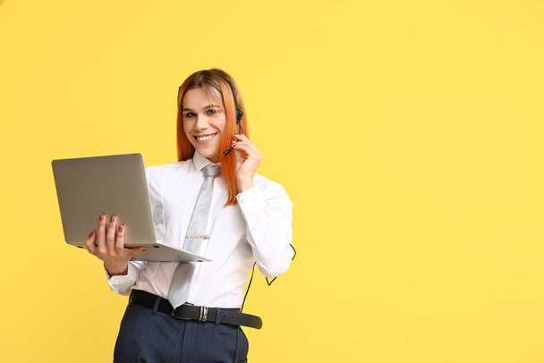 Hermosa secretaria transgénero en auriculares con portátil sobre fondo amarillo - Foto, Imagen