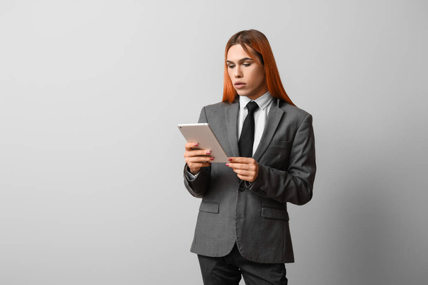 Schöne Transgender-Sekretärin mit Tablet-Computer auf grauem Hintergrund - Foto, Bild