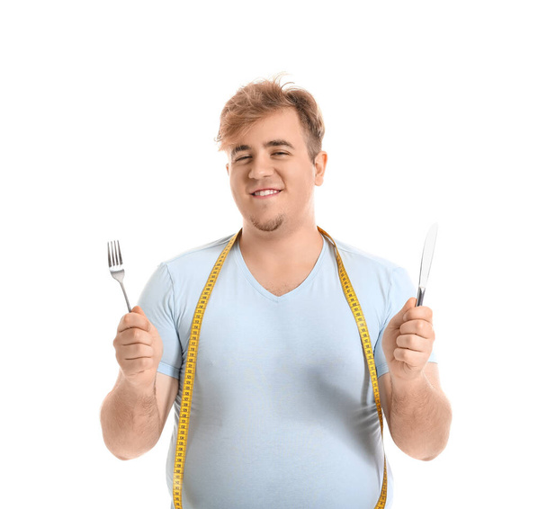 Mladý muž s nadváhou s měřicí páskou, vidličkou a nožem na bílém pozadí - Fotografie, Obrázek