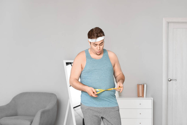 Giovane uomo sovrappeso con metro a nastro a casa - Foto, immagini