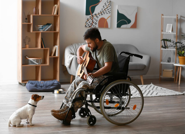 Young soldier in wheelchair playing guitar at home - Fotó, kép