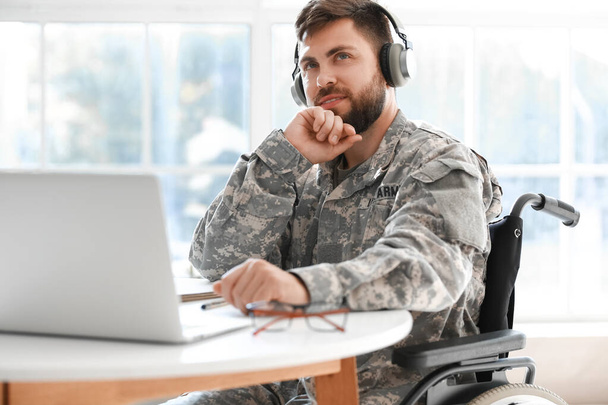 Fiatal katona tolószékben fejhallgatóval, laptoppal otthon - Fotó, kép