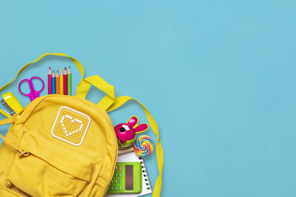 Back to school, education concept Yellow backpack with school supplies - notebook, pens, eraser rainbow, numbers isolated on blue background Top view Copy space Flat lay composition Banner. - Фото, зображення