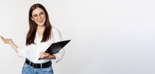 Smiling brunette woman, office lady showing way, pointing behind, demonstrating smth near her on copy space, standing over white background. - Foto, imagen