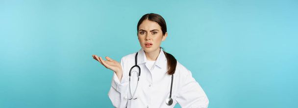 Portrait of annoyed, tired woman doctor, facepalm, roll eyes frustrated, bothered by smth stupid, standing in white coat over torquoise background. - Photo, Image