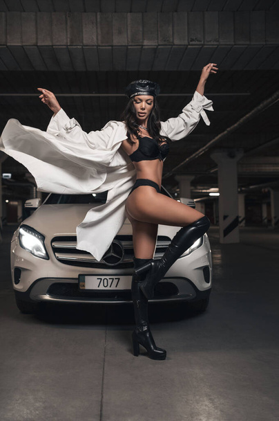 Attractive brunette in underwear and trench coat near her white car - Foto, afbeelding