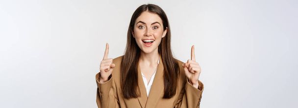 Retrato de mujer empresaria, mujer corporativa señalando con los dedos hacia arriba, sonriendo confiada, mostrando publicidad, logotipo en la parte superior, fondo blanco. - Foto, imagen
