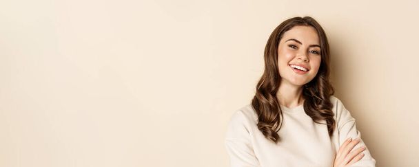 Close up portrait of young caucasian woman with dark hair, smiling white teeth, laughing, posing carefree against beige background. - Foto, afbeelding