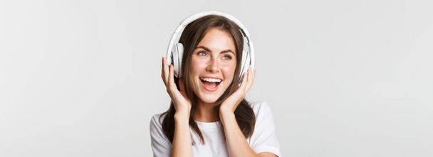 Primer plano de hermosa chica feliz sonriendo, disfrutando escuchando música en auriculares inalámbricos. - Foto, imagen