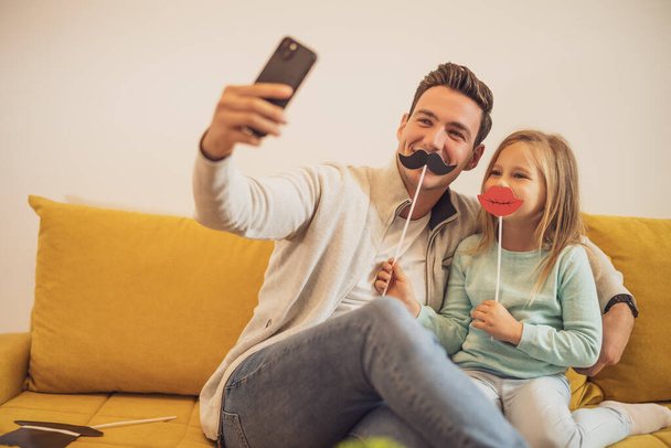 Father and daughter taking selfie while they  having fun with  party props at their home. - Foto, Imagem