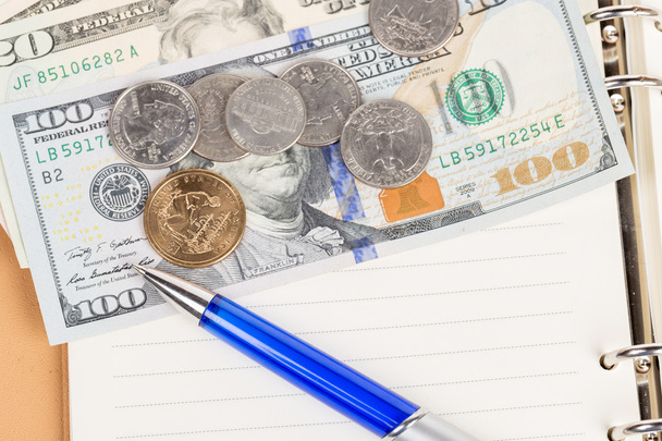 Μας κέρματα και τραπεζογραμμάτια με στυλό πάνω σε ένα σημειωματάριο - Φωτογραφία, εικόνα