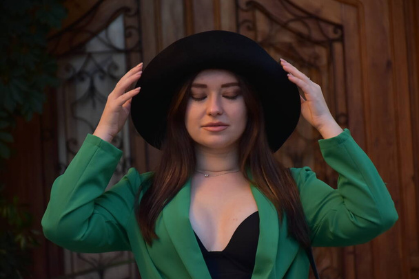 bela jovem mulher em um chapéu e vestido preto posando na cidade - Foto, Imagem