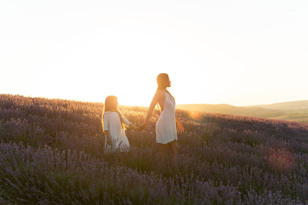 Мать и маленькая дочь на цветущем лавандовом поле на закате - Фото, изображение