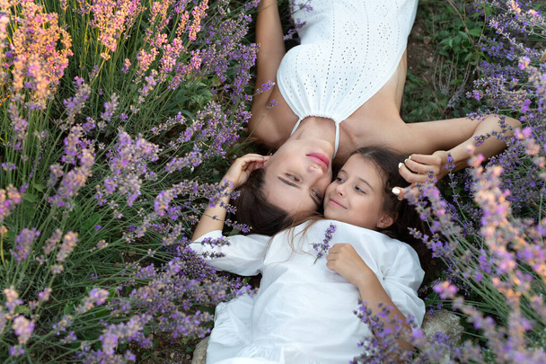 Mom and daughter in white dresses are lying in a lavender field. Provence - Foto, afbeelding