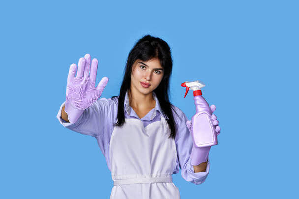 beautiful woman in rubber gloves and cleaner apron showing stop gesture isolated on blue background. focus on glove - Φωτογραφία, εικόνα