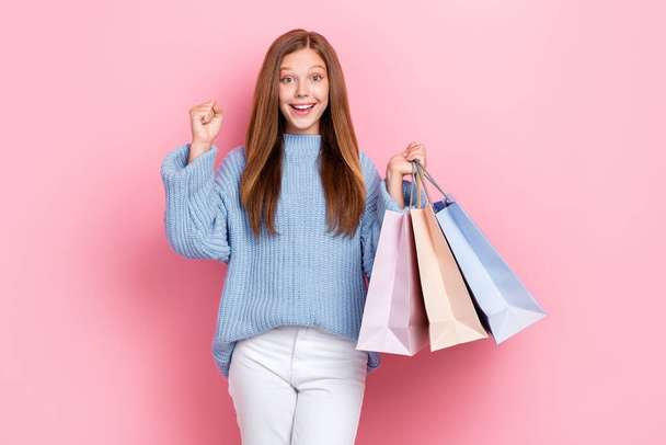 Photo poster of funny cute schoolgirl beautiful impressed positive teenager hold stack bags fists up hooray isolated on pastel pink color background. - 写真・画像