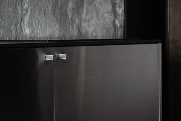 Selektivní zaměření na ocelovou kliku na moderní dveře kuchyňské skříně. Zavřít pohled na kovovou skříň v bytě ve stylu podkroví. Prvek obývacího pokoje. Interiérový design v dobře zařízeném moderním domě - Fotografie, Obrázek