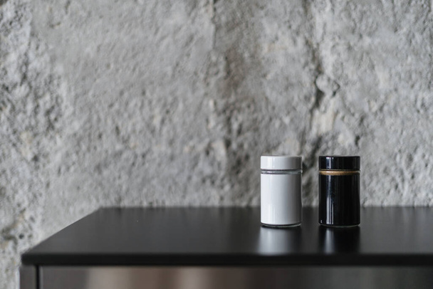 Salt and pepper shaker in black white jars standing on kitchen countertop against grey background. Spices in containers on a shelf in room with loft style design. Close up view of home decor - Foto, immagini