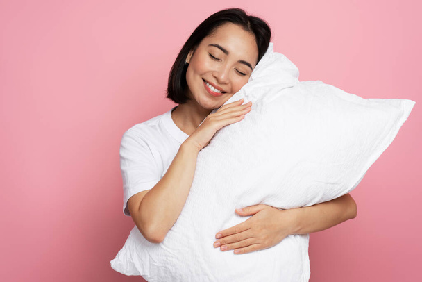 Chica hermosa satisfecha abrazando almohada con los ojos cerrados y durmiendo aislado sobre fondo de color rosa. Concepto para dormir - Foto, imagen