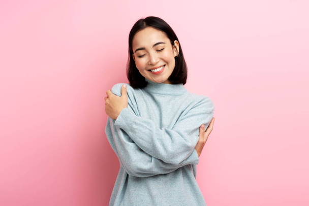 I love myself! Portrait of self-satisfied egoistic woman embracing herself and smiling with pleasure, feeling self-pride. Studio shot isolated on pink background  - 写真・画像