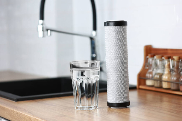 A glass of clean fresh water and carbon filter cartridge on wooden table in a kitchen interior. Installation of reverse osmosis water purification system. Concept Household filtration system - Foto, Bild
