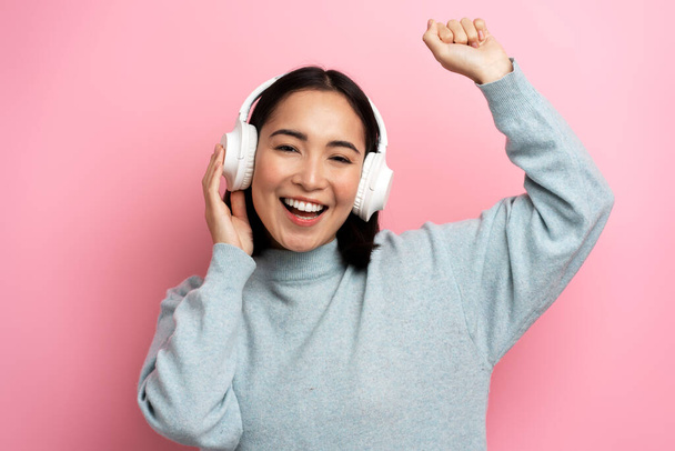 Feliz menina satisfeita dançando ouvir música favorita com fones de ouvido e dentes sorridentes, Indoor studio shot, isolado em fundo rosa  - Foto, Imagem