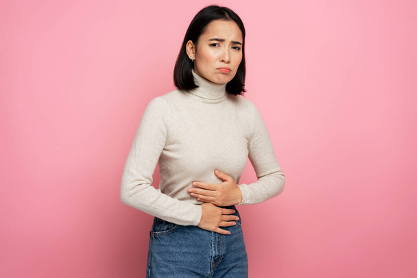 Portrait of woman clutching belly suffering stomach ache, gastritis or constipation. Indoor studio shot isolated on pink background. Abdominal pain, periods cramps concept - Photo, Image