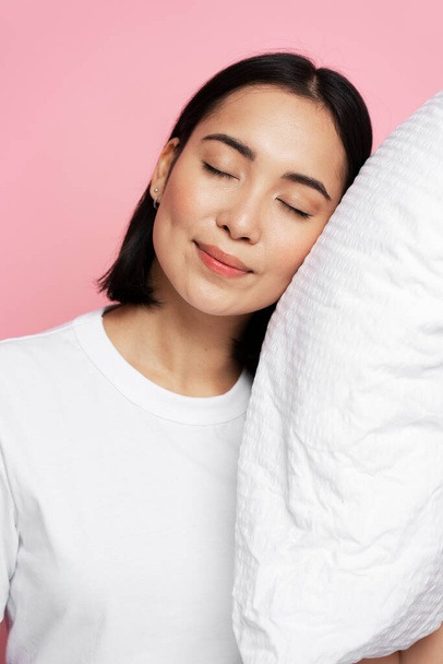 Foto portrét nádherné dívky objímající polštář se zavřenýma očima izolované na růžovém pozadí. Koncept spánku  - Fotografie, Obrázek
