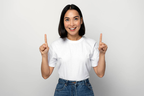 Radosna pozytywna kobieta wskazująca palcem w górę, pokazująca miejsce na twoją reklamę, mająca zębaty uśmiech. Kryty studio strzał izolowany na białym tle  - Zdjęcie, obraz