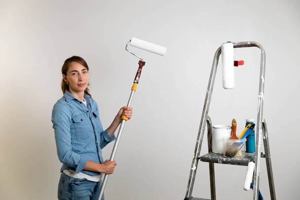 Women holding a paint roller for coloring walls, ladder with paint brushes and tools. Home improvement concept. - Zdjęcie, obraz
